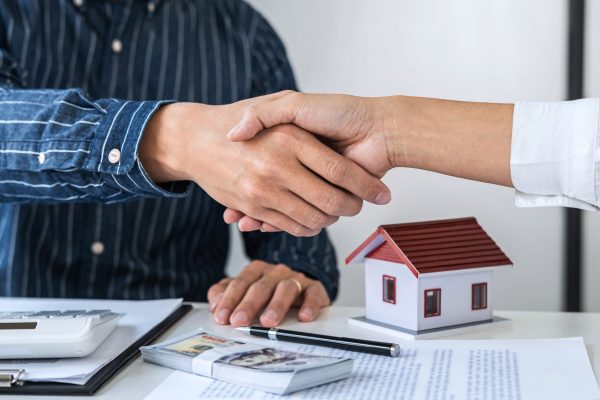 Real estate agent and customers shaking hands together celebrating finished contract after signing about home insurance and investment loan, handshake and successful deal.